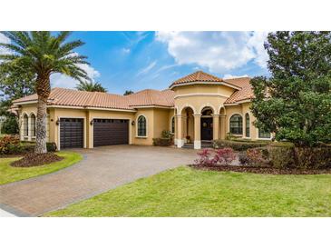 Elegant home featuring a tile roof, arched entryway, three-car garage, landscaped front yard and brick paved driveway at 11856 Vinci Dr, Windermere, FL 34786