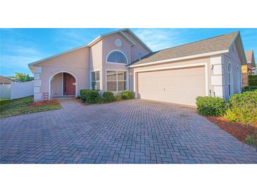 Charming single-story home with a brick driveway, arched entry, well-maintained landscaping, and attached two-car garage at 153 Cambridge Ave, Davenport, FL 33896