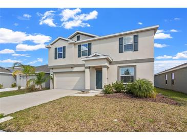 Two-story home featuring neutral colors, dark shutters, attached garage, and green landscaping under a blue, partly cloudy sky at 293 Pineywoods St, St Cloud, FL 34772