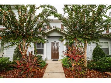 Inviting townhome entrance with a brown front door, complemented by lush landscaping and mature trees at 2962 Lucayan Harbour Cir # 102, Kissimmee, FL 34746