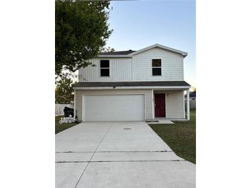 Two-story home with a two-car garage and a red front door, under a blue sky at 49 Inconnu Dr, Poinciana, FL 34759