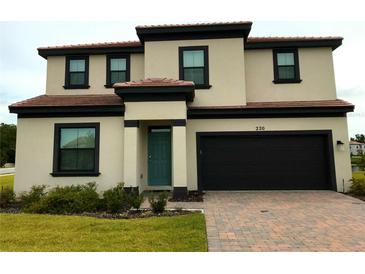 Charming two-story home featuring a brick driveway, neutral stucco, dark trim, and a teal front door at 220 Brookes Pl, Haines City, FL 33844