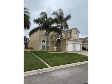 Stucco two-story home featuring a two-car garage, well-kept lawn, and tropical landscaping at 2663 Sand Hill Point Cir, Davenport, FL 33837