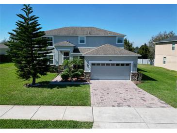 Two-story home featuring a well-manicured front lawn, paver driveway, and neutral-toned exterior with stone accents at 1336 Lattimore Dr, Clermont, FL 34711