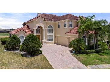 Elegant two-story home with well-manicured lawn, brick driveway, arched window, and a red tile roof at 2375 Pinehurst Ct, Davenport, FL 33837