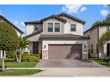 Charming two-story home featuring a manicured lawn, brick driveway, two-car garage, and attractive architectural details at 9811 Aurea Moss Ln, Orlando, FL 32832