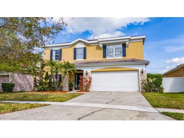 Inviting two-story home featuring a two-car garage, lush landscaping, and a sunny yellow facade at 10937 Prairie Hawk Dr, Orlando, FL 32837