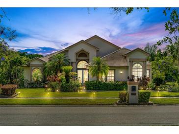 Elegant home showcasing manicured landscaping, lush palm trees, and illuminated lighting at dusk at 8550 Lost Cove Dr, Orlando, FL 32819