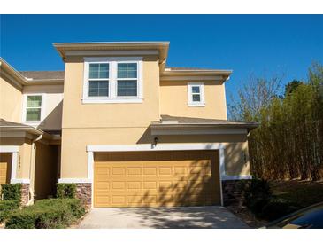 Two story tan home featuring a two car garage, manicured landscaping, and a stone facade on the bottom of the house at 17459 Chateau Pine Way, Clermont, FL 34711