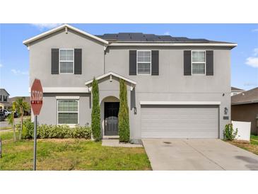 Two-story home with gray stucco, black shutters, and solar panels, complemented by well-maintained landscaping at 204 Taft Dr, Davenport, FL 33837