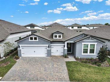 Beautiful, gray single-story home with a three-car garage and brick-paved driveway on a sunny day at 2768 Matera Dr, St Cloud, FL 34771