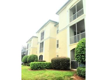 View of the three-story condo building with well-manicured landscaping and enclosed balconies at 8817 Dunes Ct # 8-303, Kissimmee, FL 34747