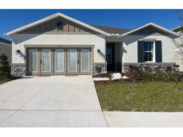 Charming single-story home featuring a stone-accented facade, well-manicured lawn, and concrete driveway at 280 Hilltop Bloom Loop, Haines City, FL 33844