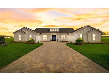 Stunning white modern farmhouse featuring a brick drive, manicured lawn, and sunset skies at 3409 Lake Diane Rd, Tavares, FL 32778