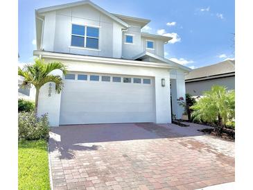 Two-story home featuring a white garage door, brick driveway and trimmed palm trees in a landscaped yard at 6608 Harper Way, Harmony, FL 34773