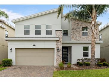 Modern two-story home boasts a neutral color scheme, stone accents, manicured landscaping, and a brick paver driveway at 581 Pebble Beach Dr, Davenport, FL 33896