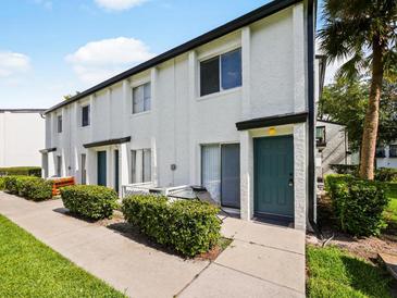 Inviting exterior featuring a well-maintained white townhome with a green door and manicured shrubbery in a garden setting at 4215 S Semoran Blvd # 15, Orlando, FL 32822