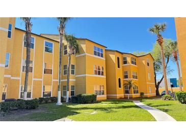 Bright yellow three-story apartment building featuring manicured landscaping, sidewalks and palm trees at 4528 Commander Dr # 2013, Orlando, FL 32822