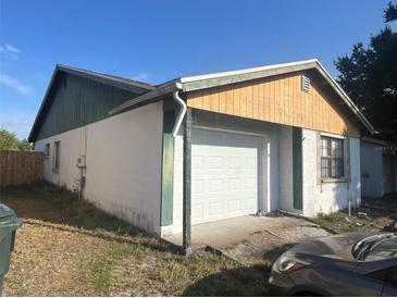 View of attached one car garage of single story home with white door and stucco siding, surrounded by lawn at 930 Buttercup Dr, Lakeland, FL 33801