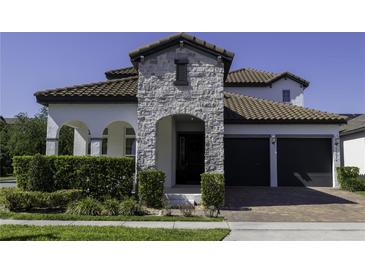 Beautiful home exterior featuring a stone facade, arched entry, and a two-car garage with a brick driveway at 15079 Guava Bay Dr, Winter Garden, FL 34787