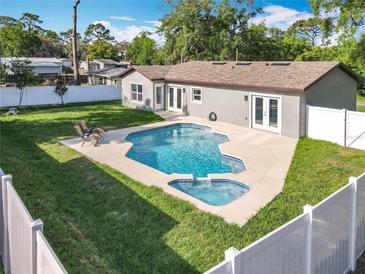 A backyard pool and spa, surrounded by a concrete deck, a well-maintained lawn, and a white fence at 7823 Bell Blvd, Orlando, FL 32810