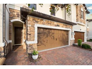 Two-car garage door nestled in a stone facade with brick paver driveway and covered entryway at 1231 Sandwedge St, Davenport, FL 33896