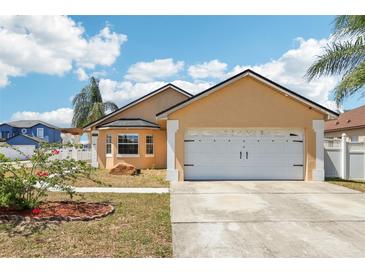 Charming tan home featuring a two-car garage, a well-maintained lawn, and a beautiful blue sky at 115 Anzio Dr, Kissimmee, FL 34758