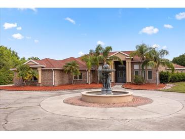 Stately brick home featuring a circular driveway, large fountain, mature landscaping, and grand entrance, with a red tile roof at 2841 S Lloyd Ln, Kissimmee, FL 34744
