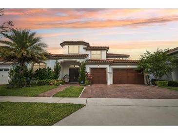 Elegant two-story home with a three-car garage, beautiful landscaping, and a brick driveway under a captivating sunset sky at 13136 Alderley Drive Dr, Orlando, FL 32832