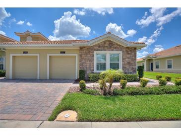 Charming villa featuring stone accents, a two-car garage, and well-maintained landscaping under a sunny, partly cloudy sky at 1082 Blackwolf Run Rd, Davenport, FL 33896