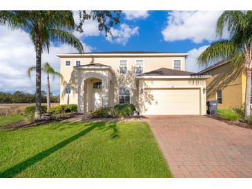 Two-story home featuring manicured lawn, palm trees, brick driveway, and a two-car garage at 389 Yellow Snapdragon Dr, Davenport, FL 33837
