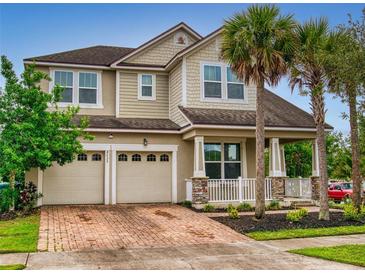 Charming two-story home featuring a brick driveway, two-car garage, and a welcoming front porch framed by columns and palm trees at 8635 Tallfield Ave, Orlando, FL 32832