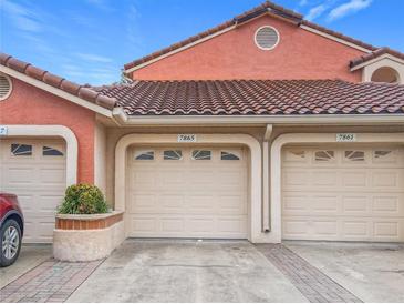 Charming condo featuring multi-car garage with neutral tone doors, orange-colored stucco, and Spanish tile roofing at 7865 Sugar View Ct # 7865, Orlando, FL 32819