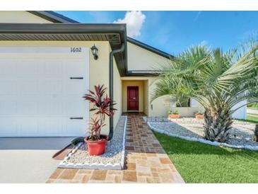 Inviting single-Gathering home features a two-car garage and a red brick walkway leading up to the red front door at 1602 Steely Dr, Dundee, FL 33838