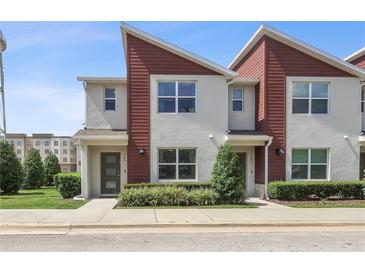 A modern townhouse with gray stucco and red siding, featuring a well-manicured lawn and inviting entrance at 185 E Warren Ave, Longwood, FL 32750