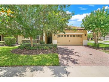 Charming single-story home with a well-manicured lawn, mature trees, and a brick-paved driveway leading to a two-car garage at 1300 Island Green St, Davenport, FL 33896