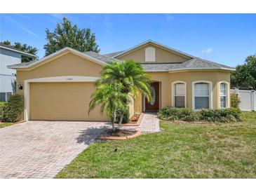 Charming single-story home featuring a well-manicured lawn, brick driveway, and a beautiful palm tree in the front yard at 15341 Groose Point Ln, Clermont, FL 34714