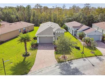 Aerial view of a well-maintained single-story home with a brick driveway, lush lawn, and mature trees at 1703 Encinitas Way, Kissimmee, FL 34759