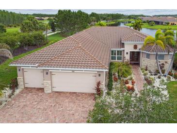 Beautiful waterfront home with brick driveway, three-car garage, tile roof, and lush tropical landscaping at 561 Tapatio Ln, Kissimmee, FL 34759