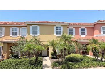 Inviting townhome featuring colorful exterior, white shutters, red tile roof, and beautiful landscaping with palm trees at 8517 Bay Lilly Loop, Kissimmee, FL 34747