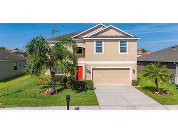 Two-story home featuring a two-car garage, well-kept lawn, mature landscaping, and a vibrant red front door at 3391 Cortland Dr, Davenport, FL 33837