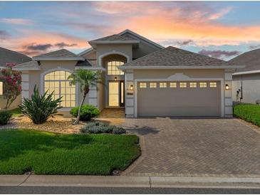 Inviting beige single-story home featuring an attached two-car garage, brick driveway, and manicured landscaping at 231 Lewis Dr, Davenport, FL 33837