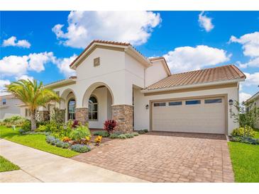 Charming stucco home with a tile roof, arched entrance, manicured lawn, and a brick-paved driveway at 13809 Abberwick Dr, Orlando, FL 32832