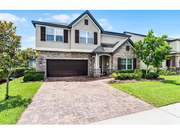 Charming two-story home with a brick driveway, stone accents, lush landscaping, and a two-car garage at 3420 Middlebrook Pl, Harmony, FL 34773