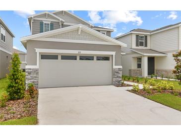 Two car garage of a gray two story home with stone veneer and manicured lawn at 212 Flag Lilly Ln, Umatilla, FL 32784
