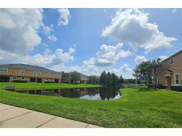 Scenic view of community pond reflecting townhouses against a blue sky with puffy clouds at 3162 Rodrick Cir, Orlando, FL 32824