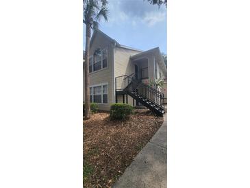 Tan two-story exterior with stairway, complemented by a mature palm tree and ground cover at 1023 S Hiawassee Rd # 4017, Orlando, FL 32835