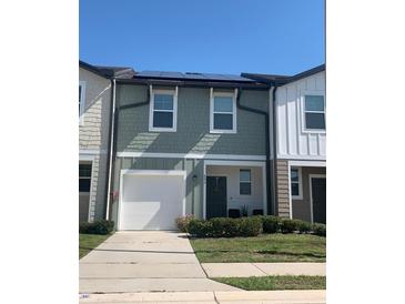 Two-story townhome featuring a one-car garage, solar panels, manicured lawn, and neutral paint at 892 Grandin St, Davenport, FL 33837
