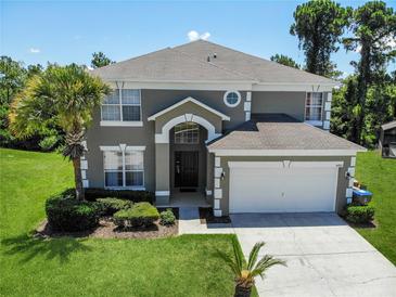 Charming two-story home featuring a well-manicured lawn, mature trees, and an attached two-car garage at 8491 Oasis Key Cv, Kissimmee, FL 34747