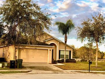 Tan single-story home with a two-car garage, palm tree, and well-maintained lawn at 2281 Royal Ridge Dr, Davenport, FL 33896